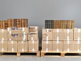 Deux piles de livres sont empilées sur des palettes devant un mur gris.