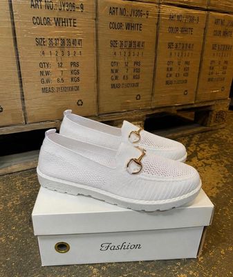 La boîte à chaussures est remplie de chaussures blanches ornées d'une boucle dorée.