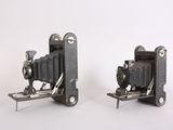 two old cameras sitting side by side on a white surface
