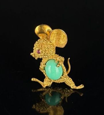 a close up of a gold mouse broochle with a green stone