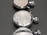 three silver and silver pocket watches are lined up on a black surface