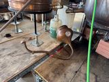 a large copper pot on a wooden table with a green hose