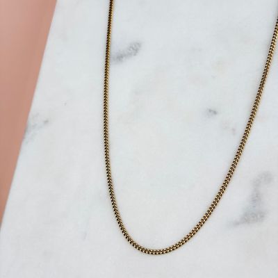 un collier à chaîne en or posé sur une surface en marbre