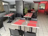 Dans un restaurant aux murs rouges, des tables et des chaises sont alignées.