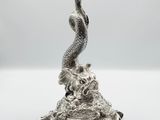 une statue en argent représentant un poisson posé sur un rocher, avec une queue de poisson
