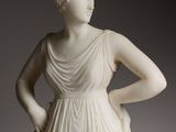 une statue représentant une femme en robe blanche, les mains sur les hanches