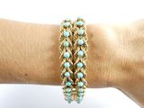 someone is holding a gold bracelet with turquoise beads on it
