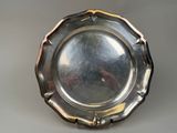 un plat ancien en argent posé sur un socle, sur une surface grise