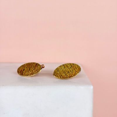 un gros plan sur une paire de boucles d'oreilles en or posées sur un bloc de marbre