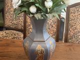a vase of flowers on a table with chairs in the background