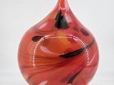 a red and black glass vase on a wooden stand