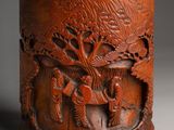 une image représentant un vase en bois orné de sculptures représentant des personnages et des arbres