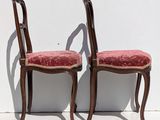 pair of wooden chairs with red upholstered cushions against a white wall