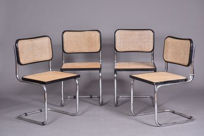 quatre chaises de salle à manger en chrome et rotin alignées sur un fond gris