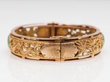 a close up of a gold bracelet with green stones on a white surface