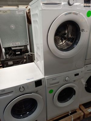 Plusieurs lave-linge et sèche-linge sont empilés sur des palettes dans un entrepôt