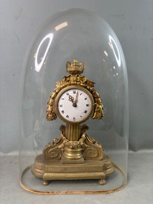 une horloge en or sous une cloche en verre, posée sur une table