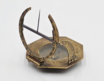 un cadran solaire doré posé sur une surface blanche, avec une paire de ciseaux