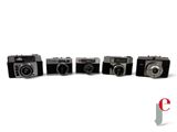 four old cameras are lined up in a row on a white surface