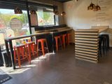 Dans un restaurant doté d'une grande baie vitrée, des tables et des tabourets sont alignés.