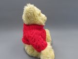 winnie the pooh stuffed animal wearing a red sweater sitting on a gray surface