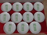 six white plates with green designs on them sitting on a red table