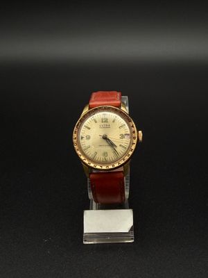 une image représentant une montre dorée et rouge posée sur un fond noir