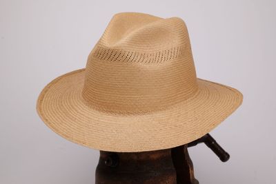 un chapeau de paille beige posé sur un porte-chapeaux en bois, devant un mur blanc