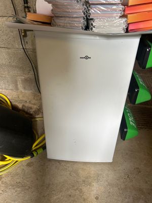 a small white refrigerator in the corner of a room next to a pile of books