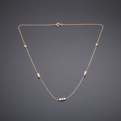 a gold necklace with pearls on a chain on a gray background