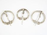 trois broches en argent posées sur une surface blanche, sur fond blanc