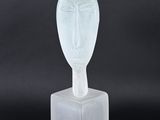 une sculpture en verre transparent représentant un visage sur un bloc