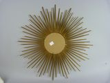 a gold sunburst hanging on the wall next to a white vase
