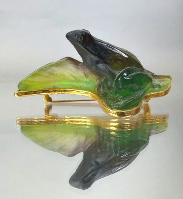 a green and black bird brooch on a gold plate
