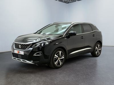 La voiture noire est garée dans une grande pièce aux murs blancs.
