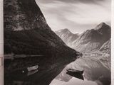 photographie en noir et blanc d'un bateau sur un lac, avec des montagnes en arrière-plan