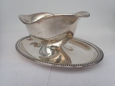 a silver sauce boat on a silver plate on a white table