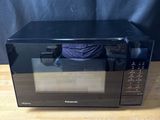 black microwave oven sitting on a wooden table with a black curtain in the background