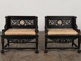 pair of black carved chairs with beige cushions on a wooden floor