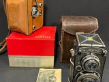 trois vieux appareils photo et une boîte remplie d'argent posés sur une table