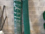 two rolls of green netting on the ground next to a brick wall