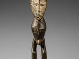 une statue en bois représentant un homme debout sur un socle noir