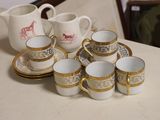 several cups and saucers are sitting on a table with a pitcher in the background