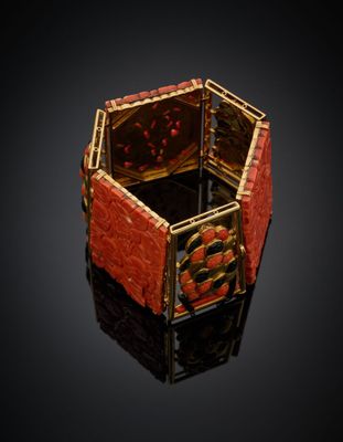 un gros plan d'une bague rouge et dorée posée sur une surface noire