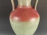 un vase orange et vert posé sur une table blanche