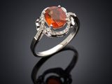 une bague sertie d'un saphir orange et de diamants, posée sur un fond noir