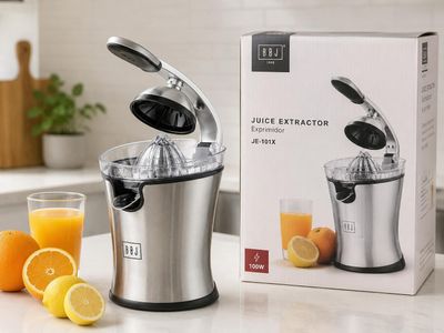 un extracteur de jus posé sur un plan de travail, à côté d'un verre de jus d'orange