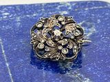 une photo d'une broche en diamant et en argent posée sur une surface en marbre bleu