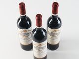 three bottles of red wine sitting next to each other on a white surface
