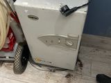 a small white refrigerator next to a cart with a hose on it